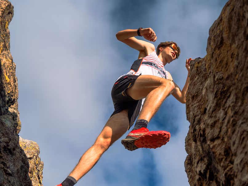 Low-angle view of a male runner in athletic gear jumping between two rocks under a blue sky.