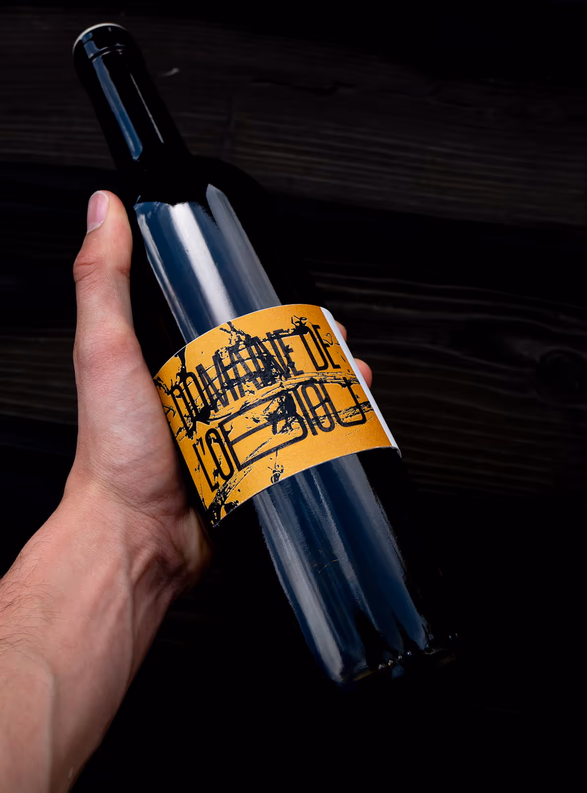 Main tenant une bouteille de vin avec une étiquette jaune Domaine de l'Obiou.