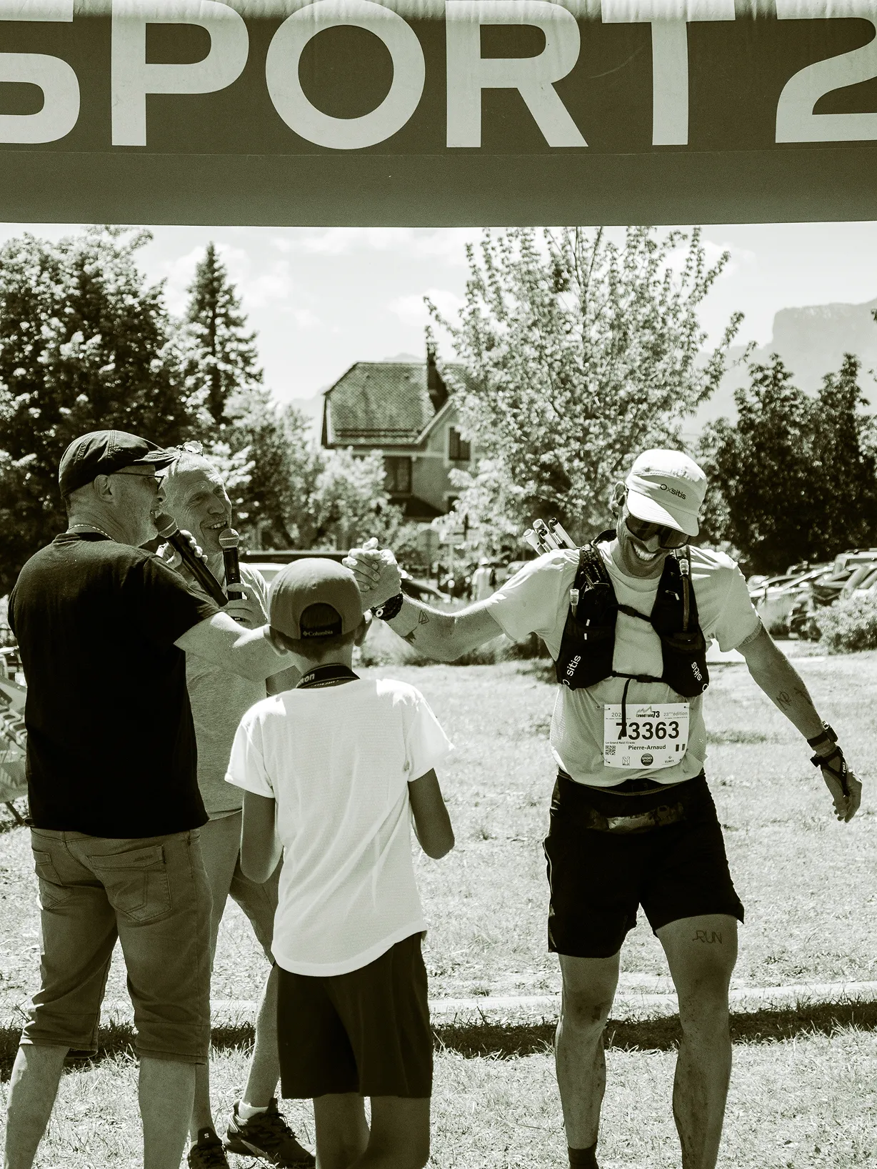 Coureur franchissant l’arche d’arrivée, félicité par un enfant et des bénévoles, ambiance sépia