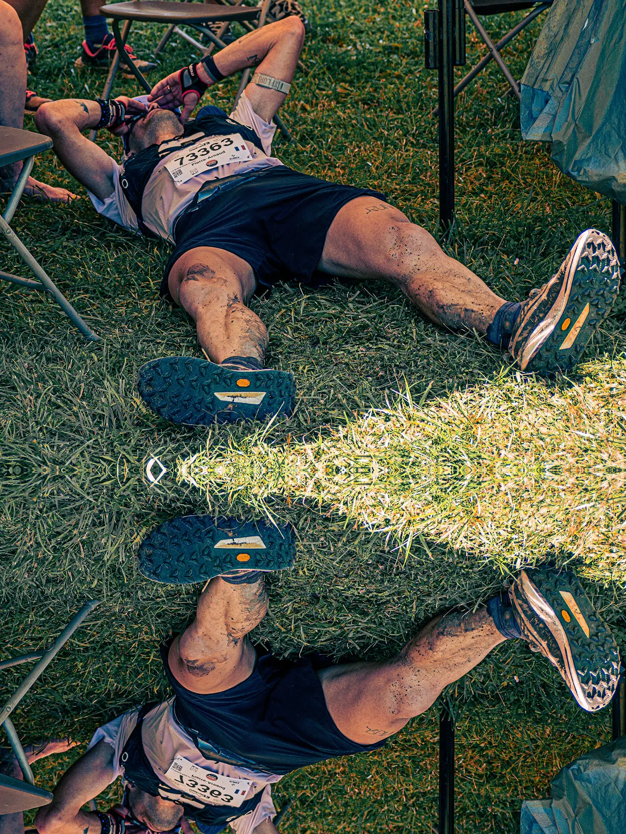 Traileur épuisé allongé dans l’herbe après la course, jambes maculées de boue, effet miroir