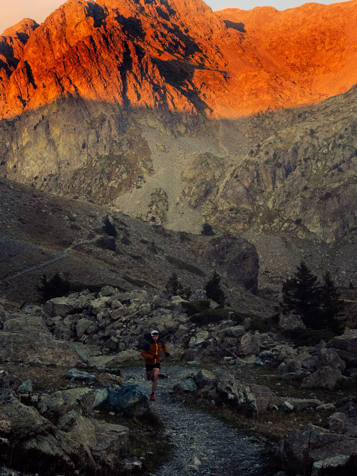 Traileur courant sur un sentier de haute montagne au lever du soleil, sommets rocheux embrasés en arrière-plan